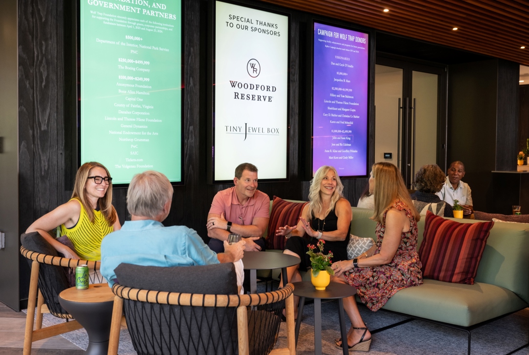 Meadow Lounge guests relax on sofas. Above them are screens displaying the names of Wolf Trap donors and partners.