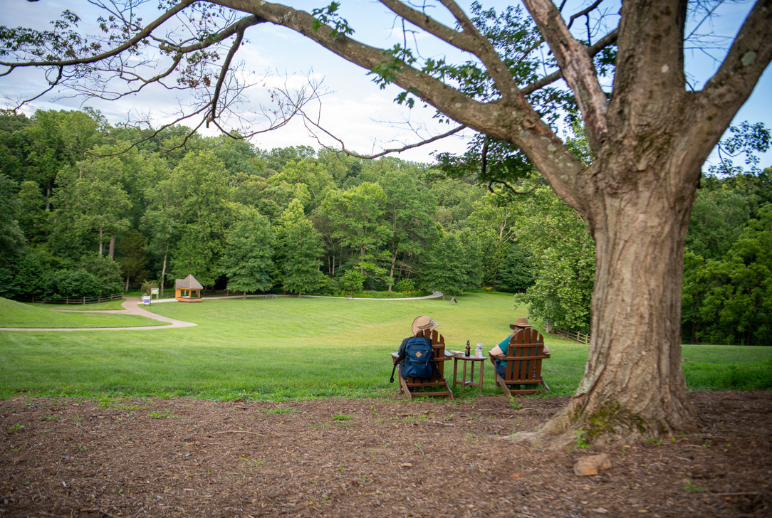 Two people relax on Adirondack chairs and look at the view of the Wolf Trap meadow.
