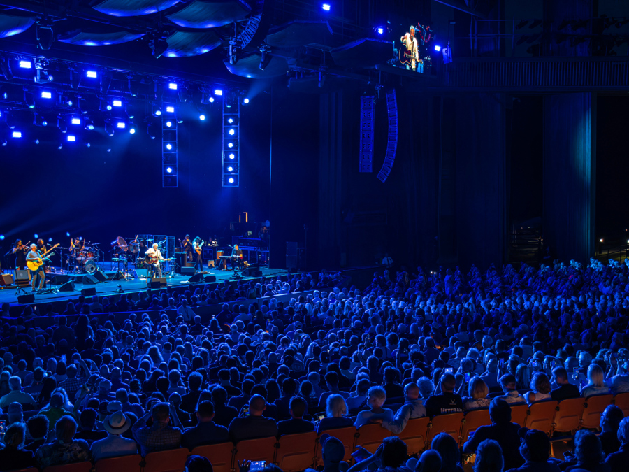 Audience watching a live performance on a blue-lit Filene Center stage.