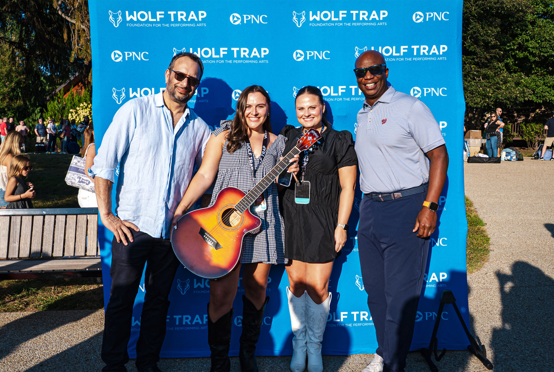 Contest winners stand in front of a Wolf Trap and PNC backdrop, one holding an acoustic guitar.