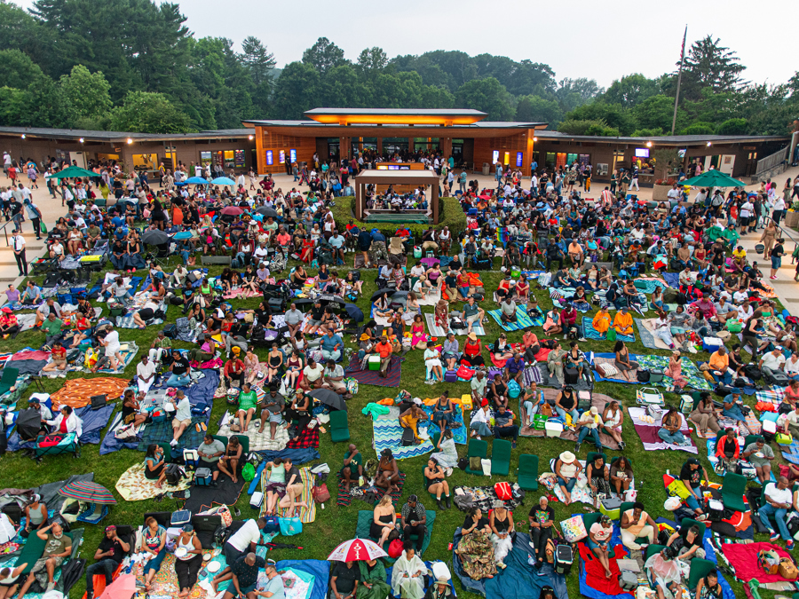 The Wolf Trap lawn covered with patrons and picnic blankets, in front of a glowing entry gate.